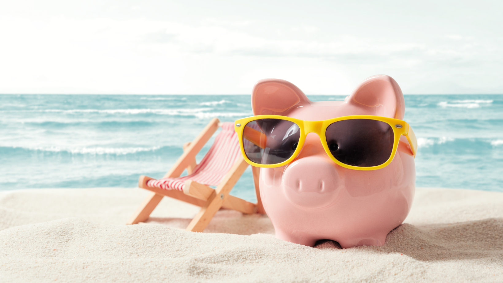 Piggy bank with sunglasses on a beach, next to a beach chair